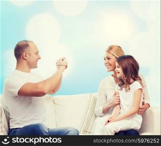 family, holidays, technology and people concept - smiling mother, father and little girl with camera over blue lights background
