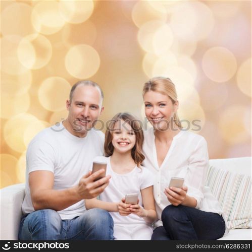 family, holidays, technology and people concept - smiling mother, father and little girl with smartphones over beige lights background