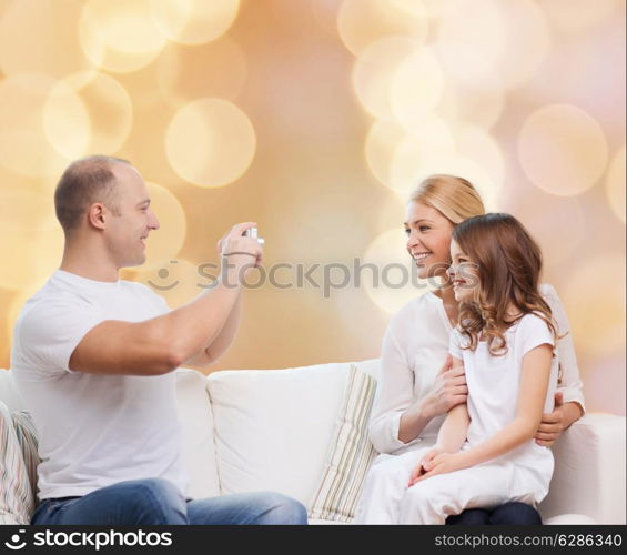 family, holidays, technology and people concept - smiling mother, father and little girl with camera over beige lights background