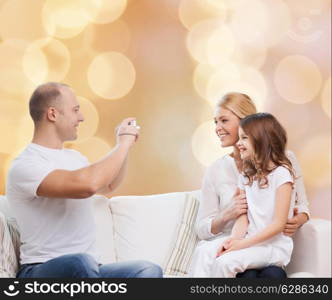 family, holidays, technology and people concept - smiling mother, father and little girl with camera over beige lights background