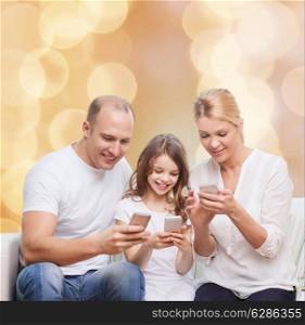 family, holidays, technology and people concept - smiling mother, father and little girl with smartphones over beige lights background