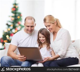 family, holidays, technology and people - smiling mother, father and little girl with laptop computer over living room and christmas tree background