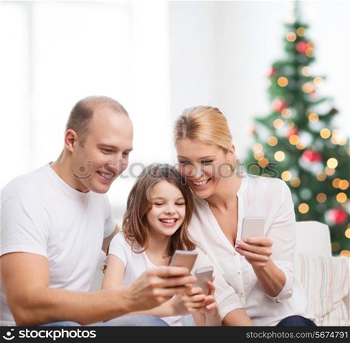 family, holidays, technology and people - smiling mother, father and little girl with smartphones over living room and christmas tree background
