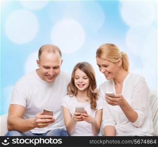 family, holidays, technology and people - smiling mother, father and little girl with smartphones over blue lights background