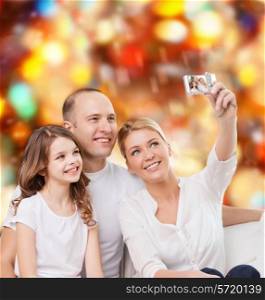 family, holidays, technology and people - smiling mother, father and little girl making selfie with camera over red lights background