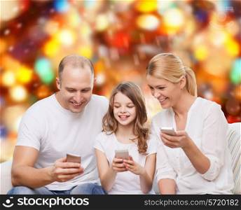 family, holidays, technology and people - smiling mother, father and little girl with smartphones over red lights background