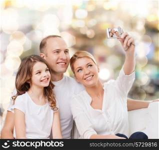 family, holidays, technology and people - smiling mother, father and little girl making selfie with camera over lights background