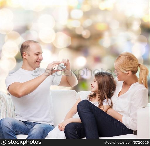 family, holidays, technology and people - smiling mother, father and little girl with camera over lights background