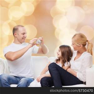 family, holidays, technology and people - smiling mother, father and little girl with camera over beige lights background