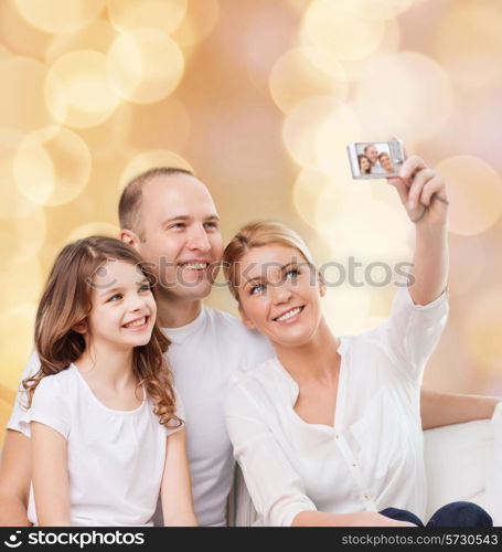 family, holidays, technology and people - smiling mother, father and little girl making selfie with camera over beige lights background