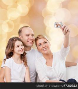 family, holidays, technology and people - smiling mother, father and little girl making selfie with camera over beige lights background