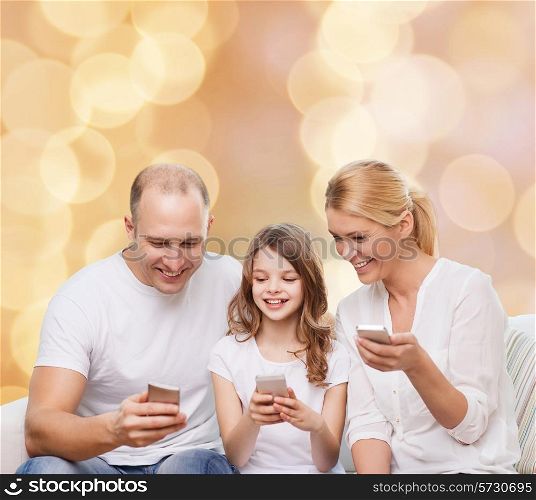 family, holidays, technology and people - smiling mother, father and little girl with smartphones over beige lights background