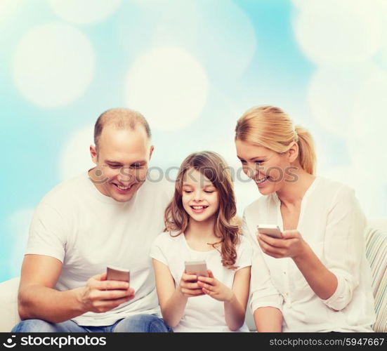 family, holidays, technology and people - smiling mother, father and little girl with smartphones over blue lights background