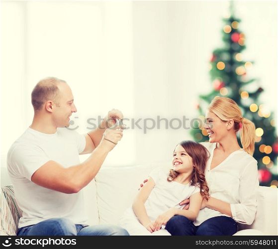 family, holidays, technology and people - smiling mother, father and little girl with camera over living room and christmas tree background