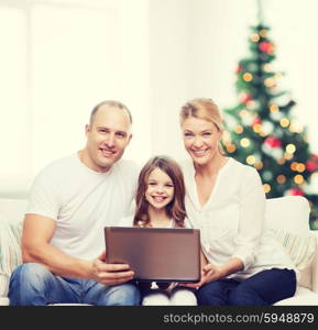 family, holidays, technology and people - smiling mother, father and little girl with laptop computer over living room and christmas tree background