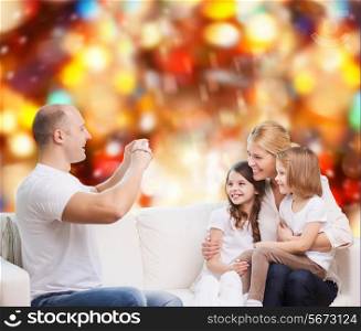 family, holidays, technology and people - smiling mother, father and little girls with camera over red lights background