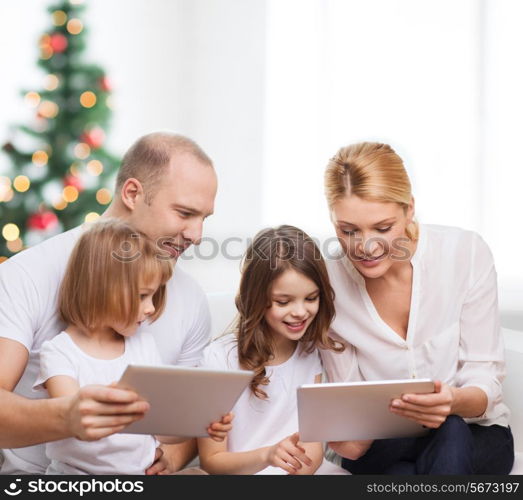 family, holidays, technology and people - smiling mother, father and little girls with tablet pc computers over living room and christmas tree background