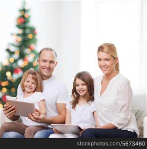 family, holidays, technology and people - smiling mother, father and little girls with tablet pc computers over living room and christmas tree background