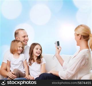 family, holidays, technology and people - smiling mother, father and little girls with camera over blue lights background