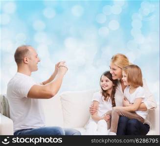 family, holidays, technology and people - smiling mother, father and little girls with camera over blue lights background