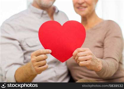 family, holidays, valentines day, age and people concept - close up of happy senior couple holding big red paper heart shape cutout at home