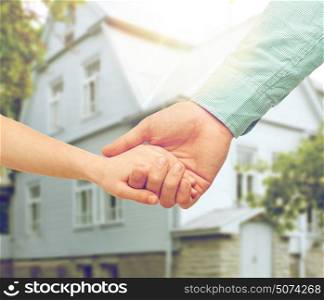 family, home and people concept - father and child holding hands over house background. father and child holding hands over house