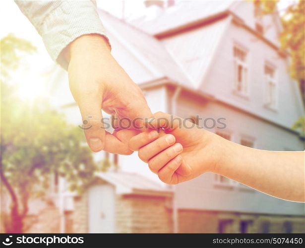 family, home and people concept - father and child holding hands over house background. father and child holding hands over house