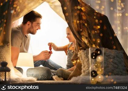 family, hygge and people concept - happy father and little daughter playing tea party in kids tent at night at home. family playing tea party in kids tent at home