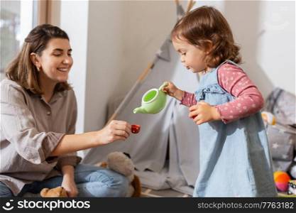 family, hygge and people concept - happy mother and little daughter playing tea party at home. mother and daughter playing tea party at home