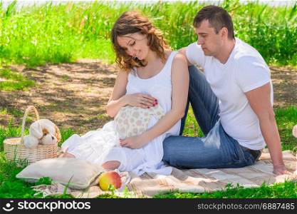 Family in anticipation of a child, rest near a lake in a park on a picnic
