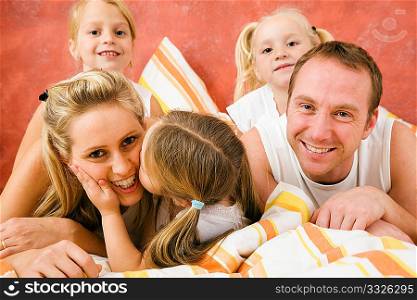 Family in bed in the morning, daughter kissing and hugging her mother