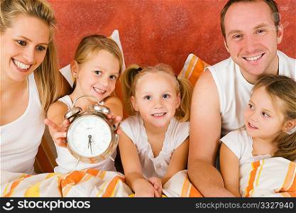 Family in bed in the morning, on child holding a clock ? metaphor for getting up to enjoy the day