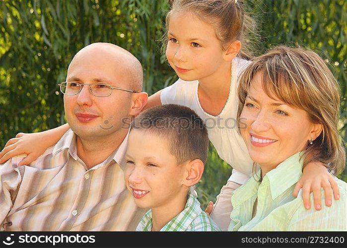 family in early fall park. dad, mom and little boy sitting at the grass. little girl is standing behind their. all of them is looking away