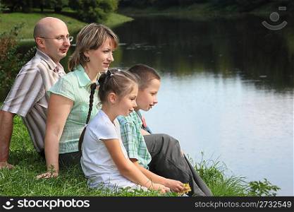 family in early fall park. father, mother, little boy and girl is sitting near pond.