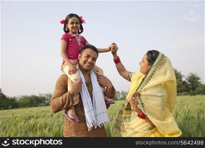 Family in field with girl on father&rsquo;s shoulders