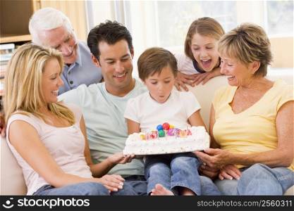 Family in living room smiling with young boy blowing out candles on cake