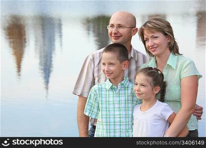 family in park. father, mother, little girl and little boy on pond background. man is embracing his wife
