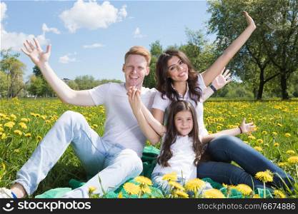 Family in park. Portrait of happy smiling family of parents and girl sitting on grass with dandelion flowers at sunny summer day