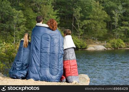 Family in sleeping bags by lake