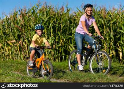 Family is cycling on their bicycles in summer - here mother with son