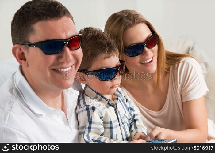 Family laughing while watching television together in the living-room wearing 3d glasses