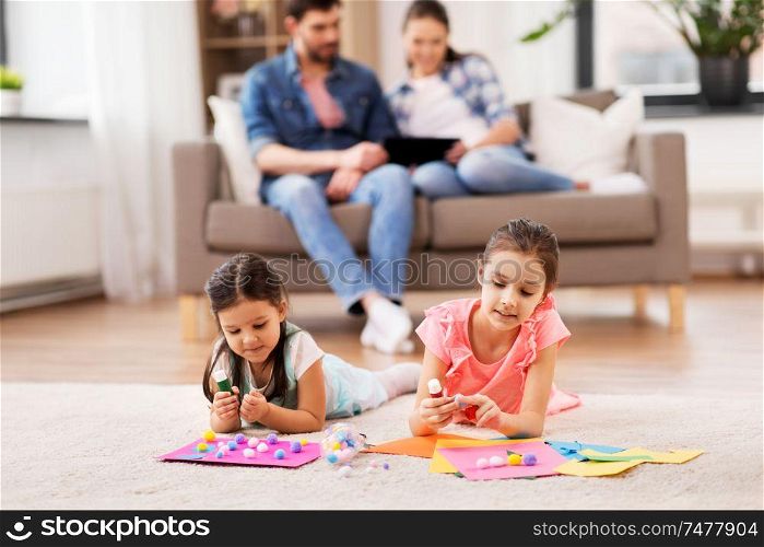 family, leisure and childhood concept - happy sisters doing arts and crafts at home. happy sisters doing arts and crafts at home