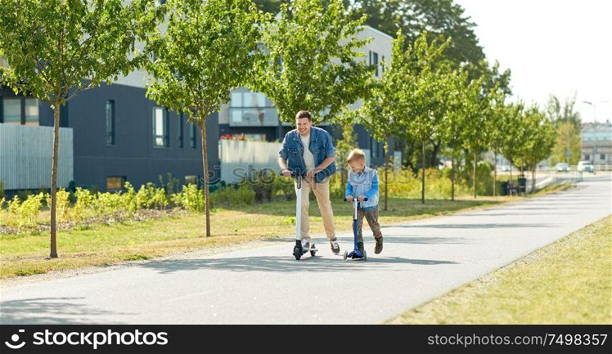 family, leisure and fatherhood concept - happy father and little son riding scooters together in city. father and little son riding scooters in city