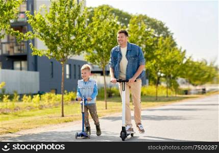 family, leisure and fatherhood concept - happy father and little son riding scooters together in city. father and little son riding scooters in city