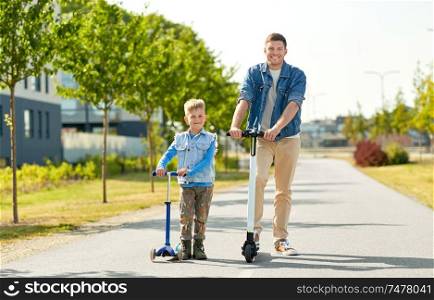 family, leisure and fatherhood concept - happy father spending time with little son riding scooters in city. father and little son riding scooters in city