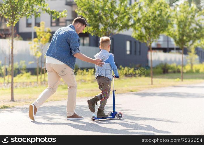 family, leisure and fatherhood concept - happy father spending time with little son riding scooter in city. happy father and little son riding scooter in city