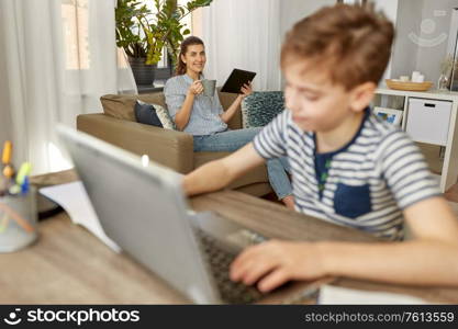 family, leisure and lifestyle concept - mother with tablet pc computer drinking coffee and son learning at home. mother with tablet pc and son learning at home