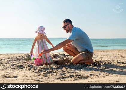 family, leisure and people concept - father and baby daughter playing with sand toys on summer beach. father and daughter playing with toys on beach