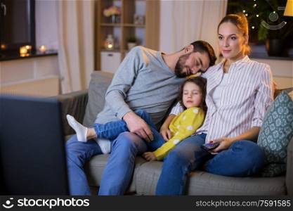 family, leisure and people concept - father and little daughter sleeping while mother watching tv at home at night. tired sleepy family watching tv at home at night