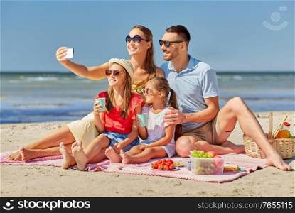 family, leisure and people concept - father, mother and two little daughters taking selfie with smartphone on summer beach. happy family taking selfie on summer beach